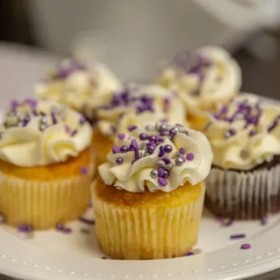 a plate of cupcakes with white frosting and purple sprinkles
