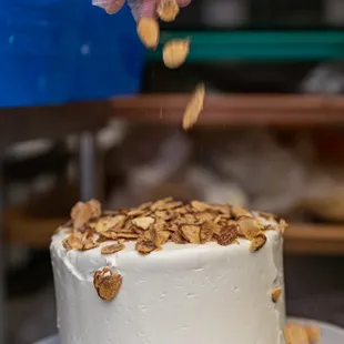 a hand sprinkling nuts onto a cake