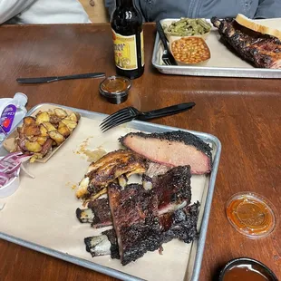 Tin roof platter with potatoes, lean brisket, chicken, and ribs.  Background is baby back ribs with green beans and bbq beans