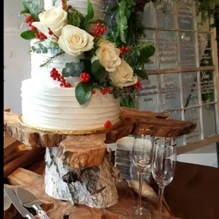 Buttercream textured cake for a holiday wedding adorned with white roses, greenery and red berries!