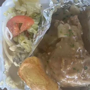 Smothered pork chops with gravy. Mashed potatoes with gravy. Cabbages topped with a tomato.