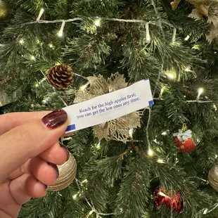 a hand holding a piece of paper in front of a christmas tree