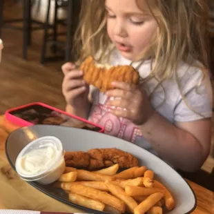a little girl eating a fried chicken sandwich