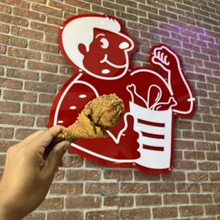 Holding piece of chicken in front of logo