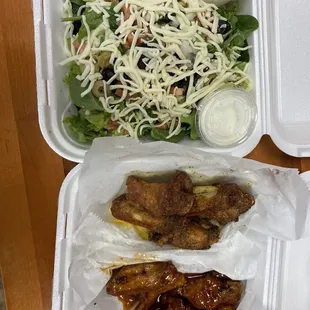a salad and chicken wings in a styrofoam container