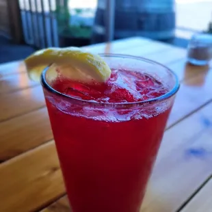 a glass of red drink with a lemon wedge