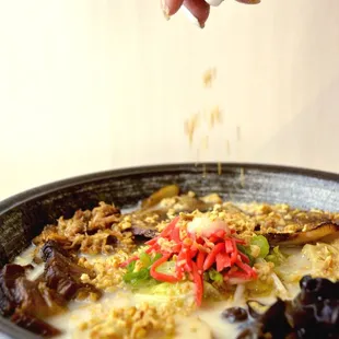 a hand sprinkling a spoon over a bowl of soup