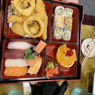 Bento box with tempura vegetables and fish sushi and sushi rolls and fruit slices
