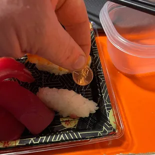 a person putting a coin on a plate of sushi