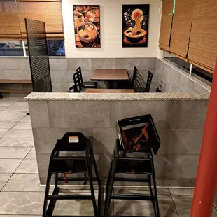 Inside the restaurant, there are six tables for 4. High chairs. Framed ramen art.
