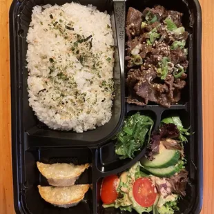 a bento box with rice, meat and vegetables