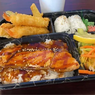 Salmon bento box with tempura, california rolls and salad.
