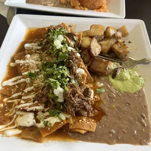 Chilaquiles de birria with some home potatoes and beans Back plate is my partners and it&apos;s enchiladas zuisas with rice and beans