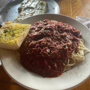 Spaghetti with meat sauce. Spinach artichoke breadsticks in the background.