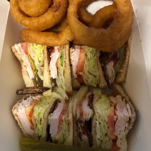 clubhouse sandwich with onion rings in to go container. simple and nice. it is as described, which makes this dish and meal good