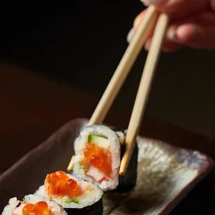 a person holding chopsticks over a plate of sushi