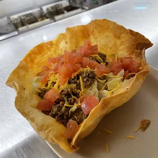 Taco salad served in an edible bowl with beef, lettuce, tomato, onion, and shredded cheddar cheese $11.99