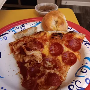Slice of pie with a garlic roll showing. In the cup is the Italian dressing/oil for the sub.