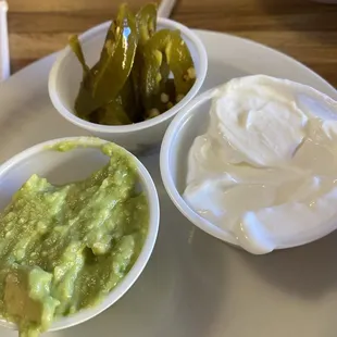 two bowls of guacamole and a bowl of sour cream
