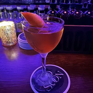 a drink in a coupe glass with an orange garnish