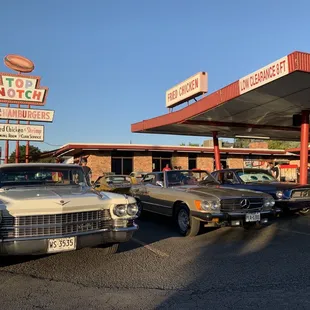 several classic cars parked in front of a gas station
