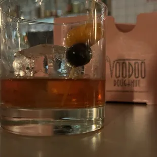 a glass of whiskey with an olive on the rocks