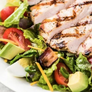a salad with chicken, lettuce, tomatoes, and avocado