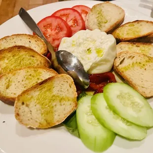 a plate of bread, tomatoes, cucumbers, and a spoon