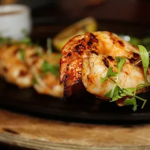 The Mojo Grilled Prawns are grilled and served on a skillet with shishito peppers &amp; lemon on the side.