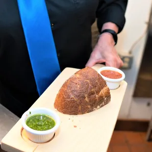 a man holding a loaf of bread and dipping sauces