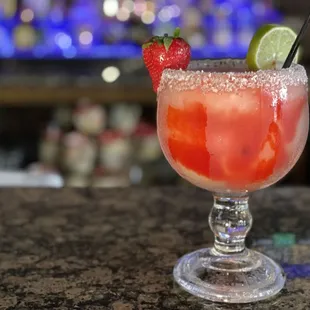 a cocktail with a strawberry and lime garnish