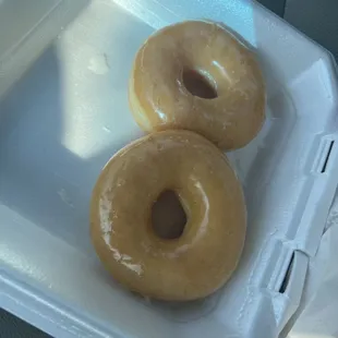 two glazed donuts in a styrofoam container