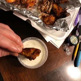 a hand dipping a piece of chicken wings