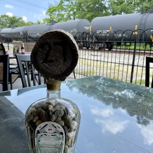 a bottle of coins on a table with a train in the background