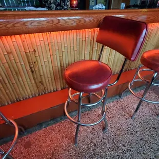 three red stools in front of a bamboo bar