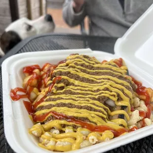 a takeout container with a hot dog covered in ketchup and mustard