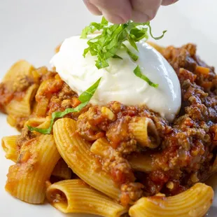 a person putting a dollop of sour cream on top of a pasta dish