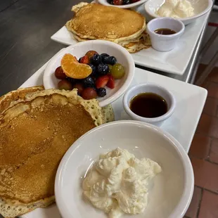 Buttermilk pancakes topped with Chantilly cream and maple syrup with a side of mixed fruit.