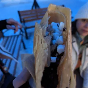 a woman holding a hot dog with marshmallows