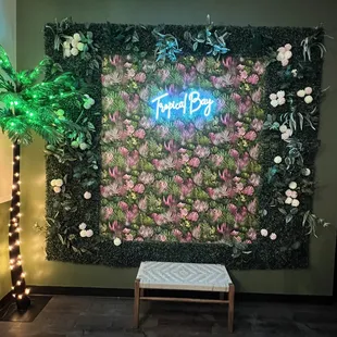 a wall of plants with a neon sign