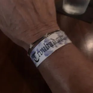 a man's wrist with a wristband that reads troubadour