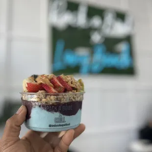 a hand holding a bowl of fruit and yogurt