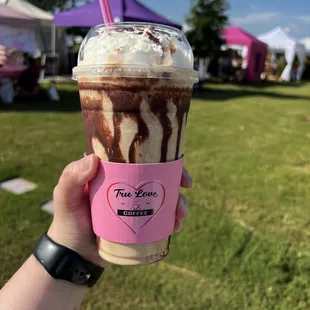 A chocolate lined coffee cup filled with a blended iced coffee drink that&apos;s topped with whipped cream and a pink straw.