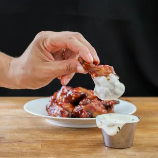 a hand dipping a piece of chicken wings