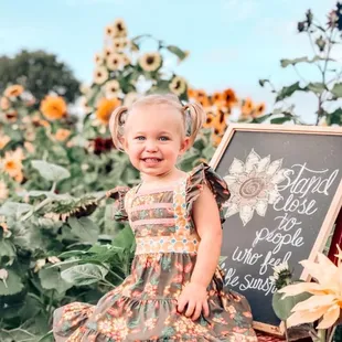 a little girl sitting in a field of sunflowers
