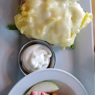 Delish breakfast bagel with egg &amp; cheese with fixings, fresh fruit cup sprinkled with powdered sugar.