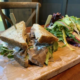 Warm roast beef sandwich with side salad.