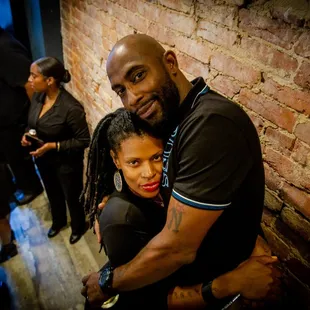 a man and a woman hugging in front of a brick wall