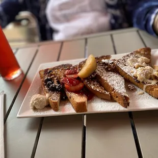 a plate of french toast with fruit and powdered sugar