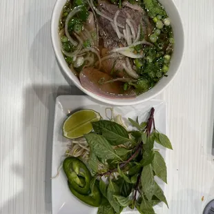 a bowl of beef pho garnished with herbs